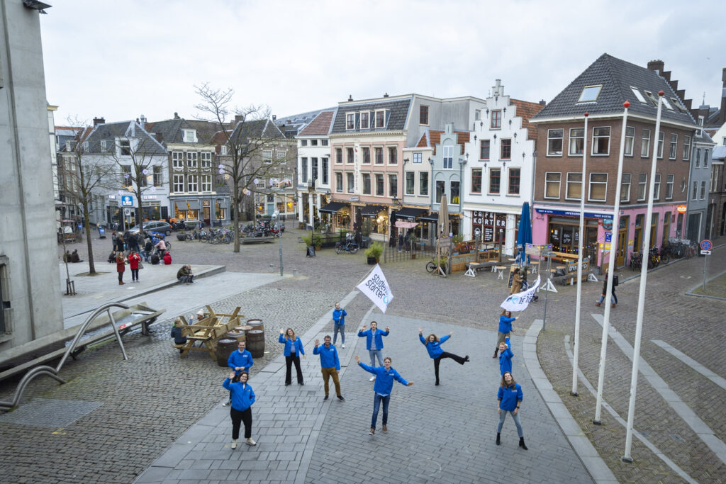 Enthousiaste leden in blauwe jassen van boven gefotografeerd op stadhuisplein